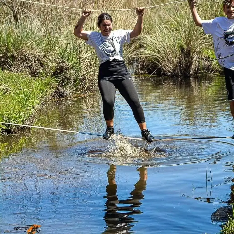 Participante cruzando la cañada sobre una cuerda, brazos en alto
