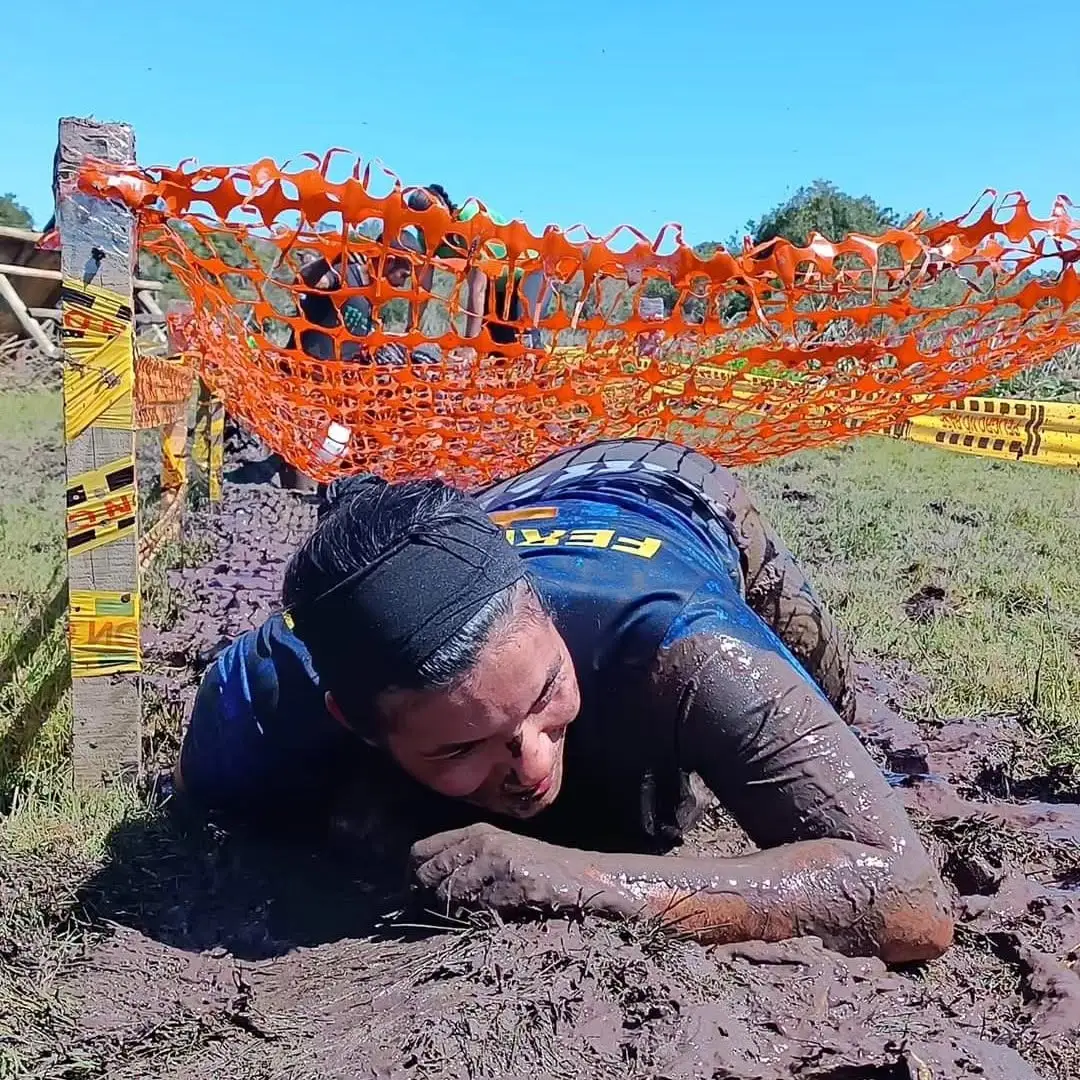 Participante arrastrándose por el barro bajo la red naranja