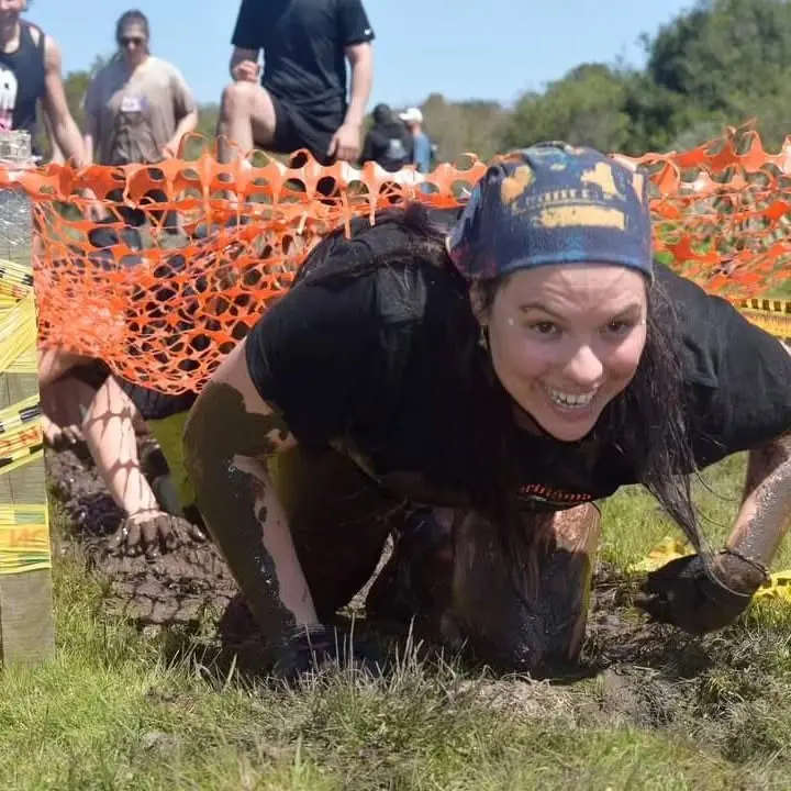 Participante avanzando en el barro bajo la red naranja, sonriendo