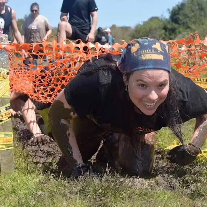 Participante avanzando en el barro bajo la red naranja, sonriendo